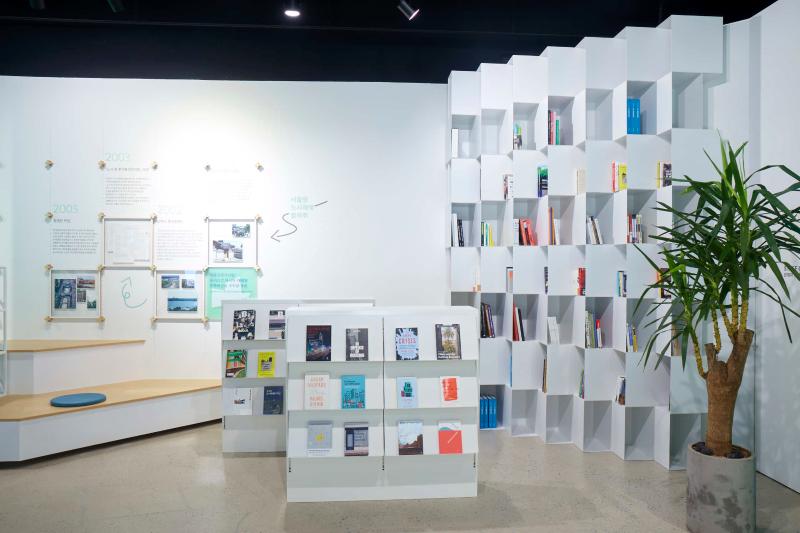 Bookshelves and a reading area sit behind a plant.