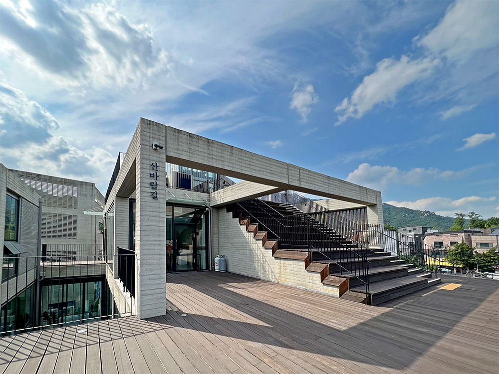 Bukhansan Mountain can be seen behind the concrete pavilion surrounded by wooden stairs.