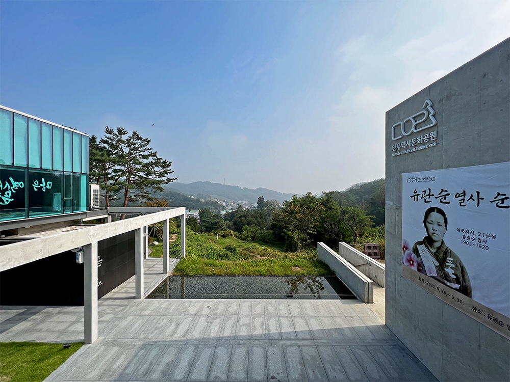 There's a building on the left side and a large concrete wall on the right side. Between them, there's a shallow pool of water and a wide Mangusan Mountain is stretched out in the background.