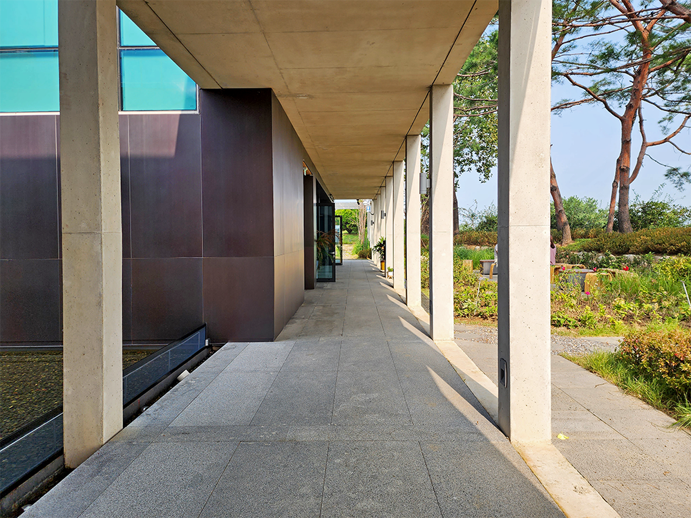 Thin rectangular pillars stand in an evenly-spaced line at the right side of the long passageway.