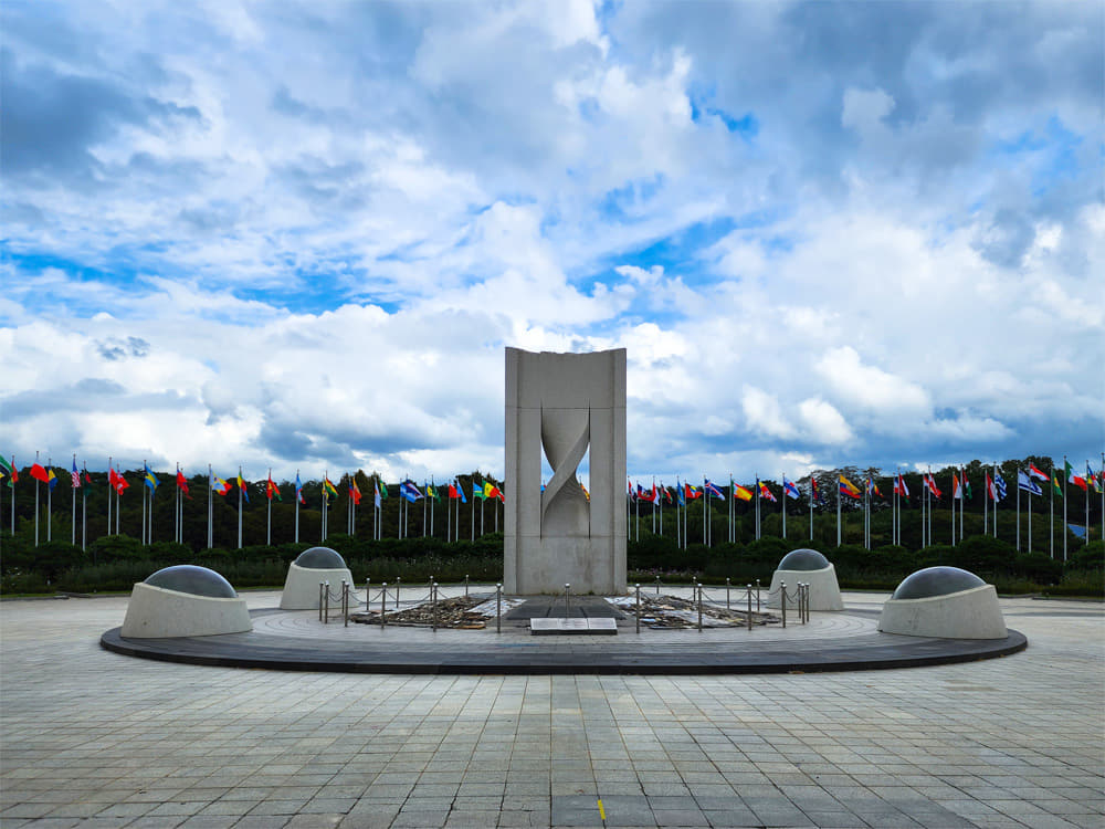 Flags of all nations lined up behind a large memorial sculpture.