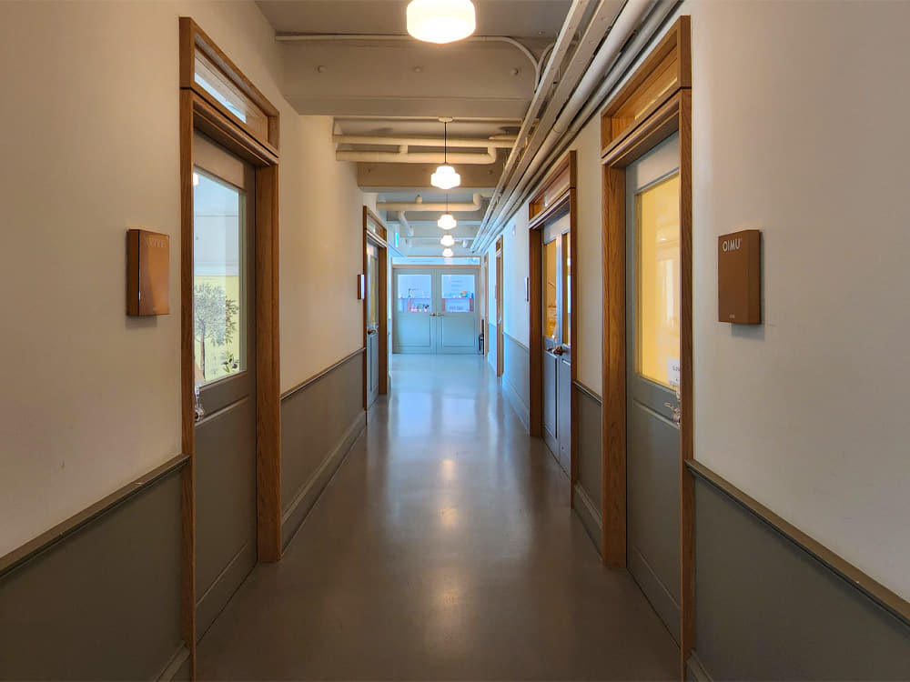 Green doors with wooden frames face each other on either side of a long corridor