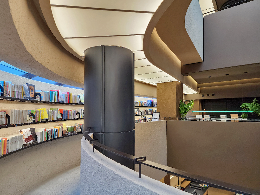 Books displayed on the wall to the left side of a thick iron pillar, and a railing on the right